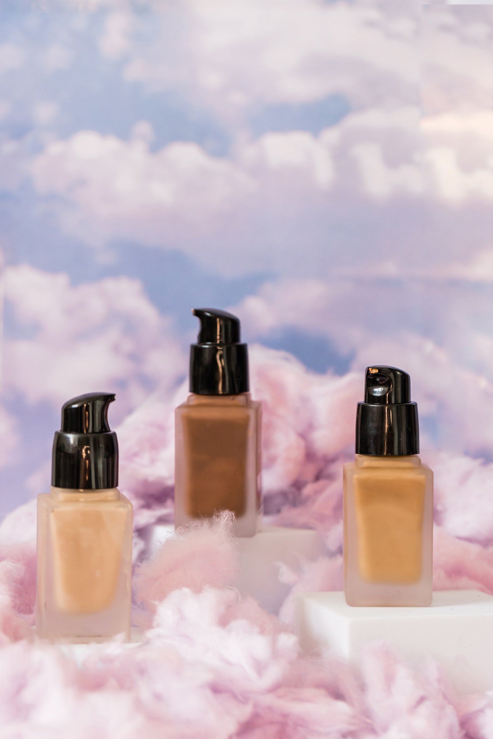 Cushion foundation bottles staged against a soft pastel cloud backdrop